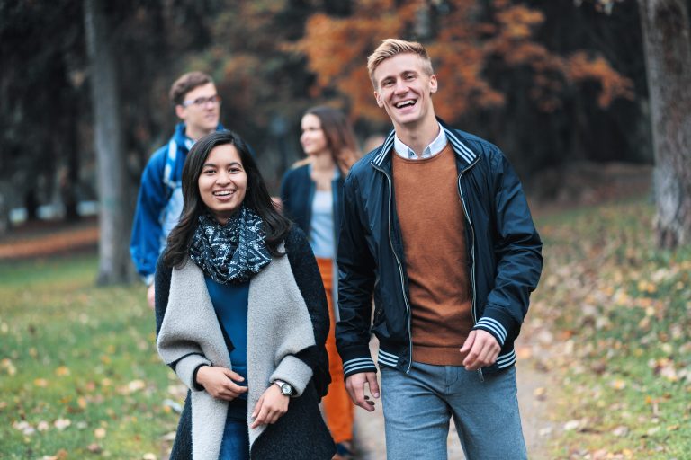 Hymyileviä opiskelijoita kävelemässä kameraa kohti syksyisessä maisemassa.