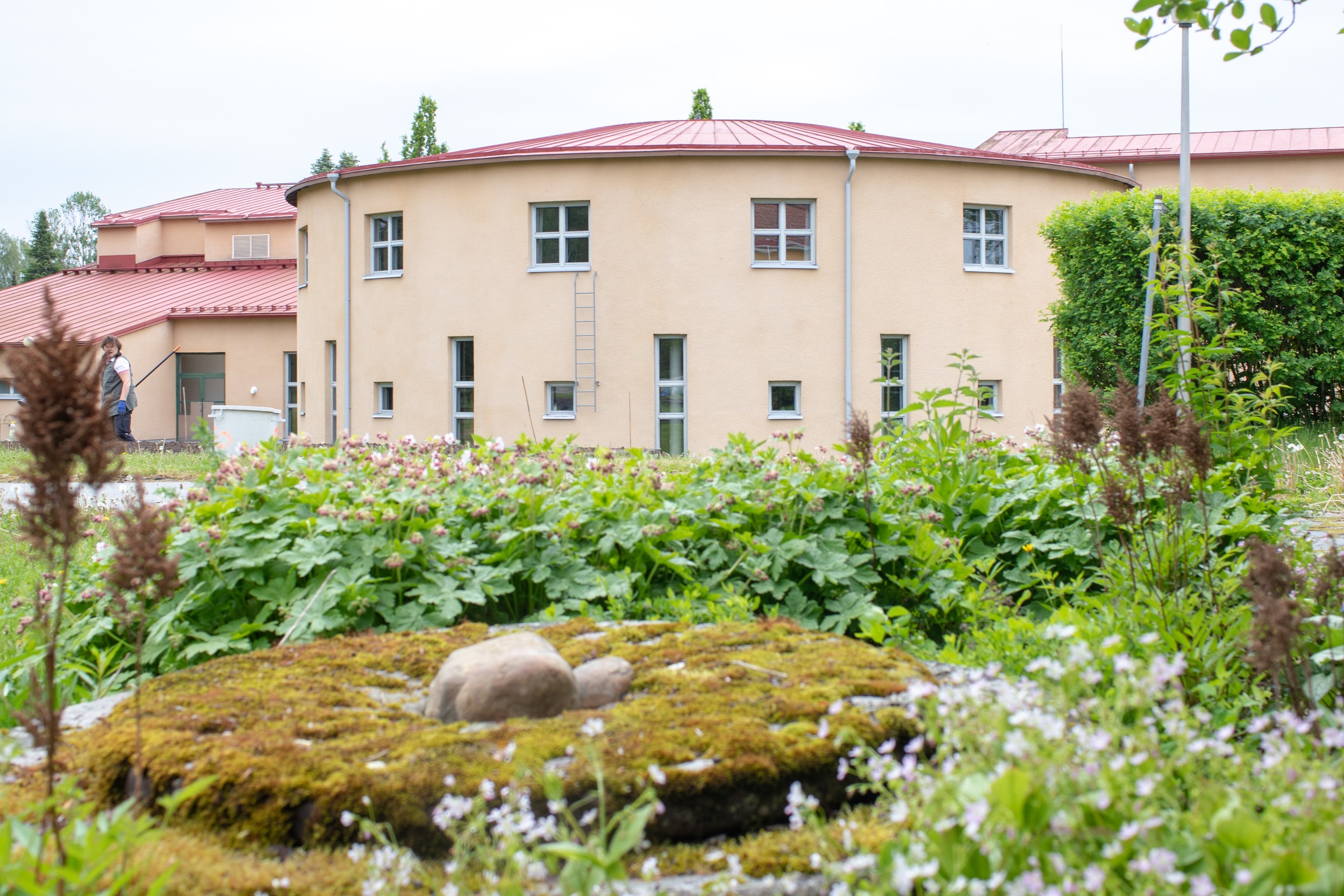 Lepaan kampuksen päärakennus. Rakennus on vaalean kerman värinen ja pyöreä. Etualalla vihreitä istutuksia. 