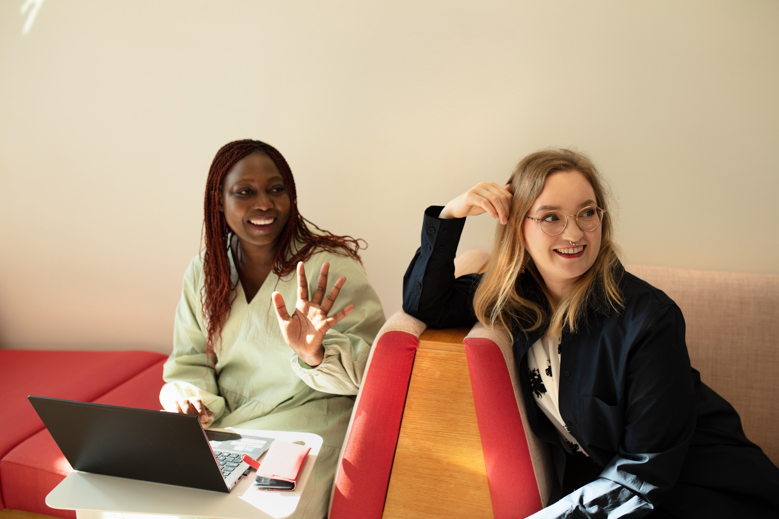 Two people are looking out of the picture to the right and smiling. One of them has a laptop on their lap, and they are sitting on a sofa.