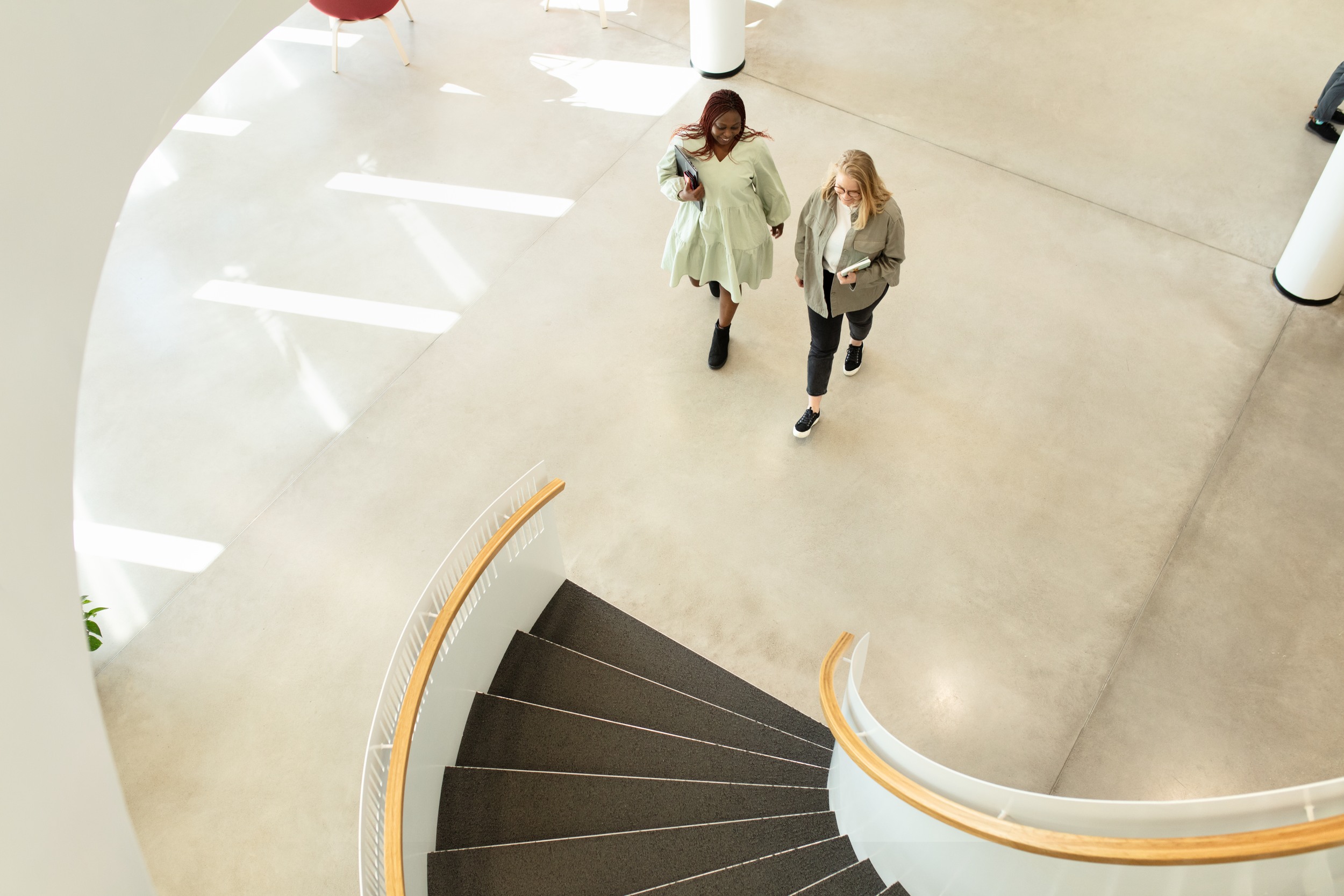 Two individuals are walking towards the lobby stairs. The individuals are captured from an overhead perspective.