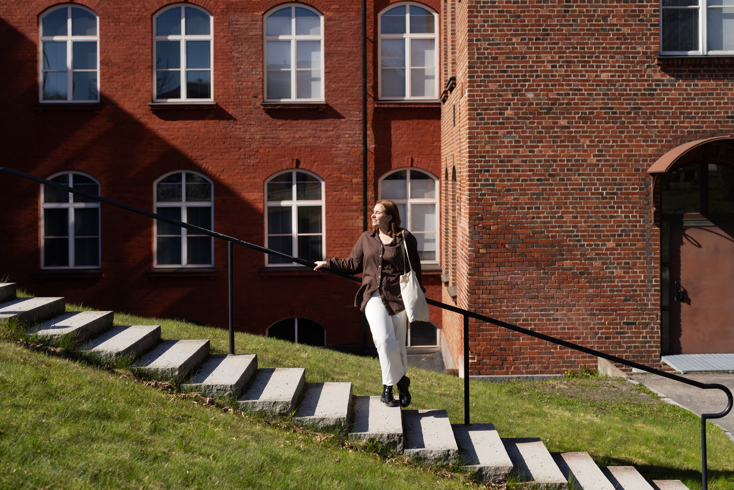 A spring day at the Forssa campus, the sun is shining. A woman is standing on the stairs and leaning on the railing.