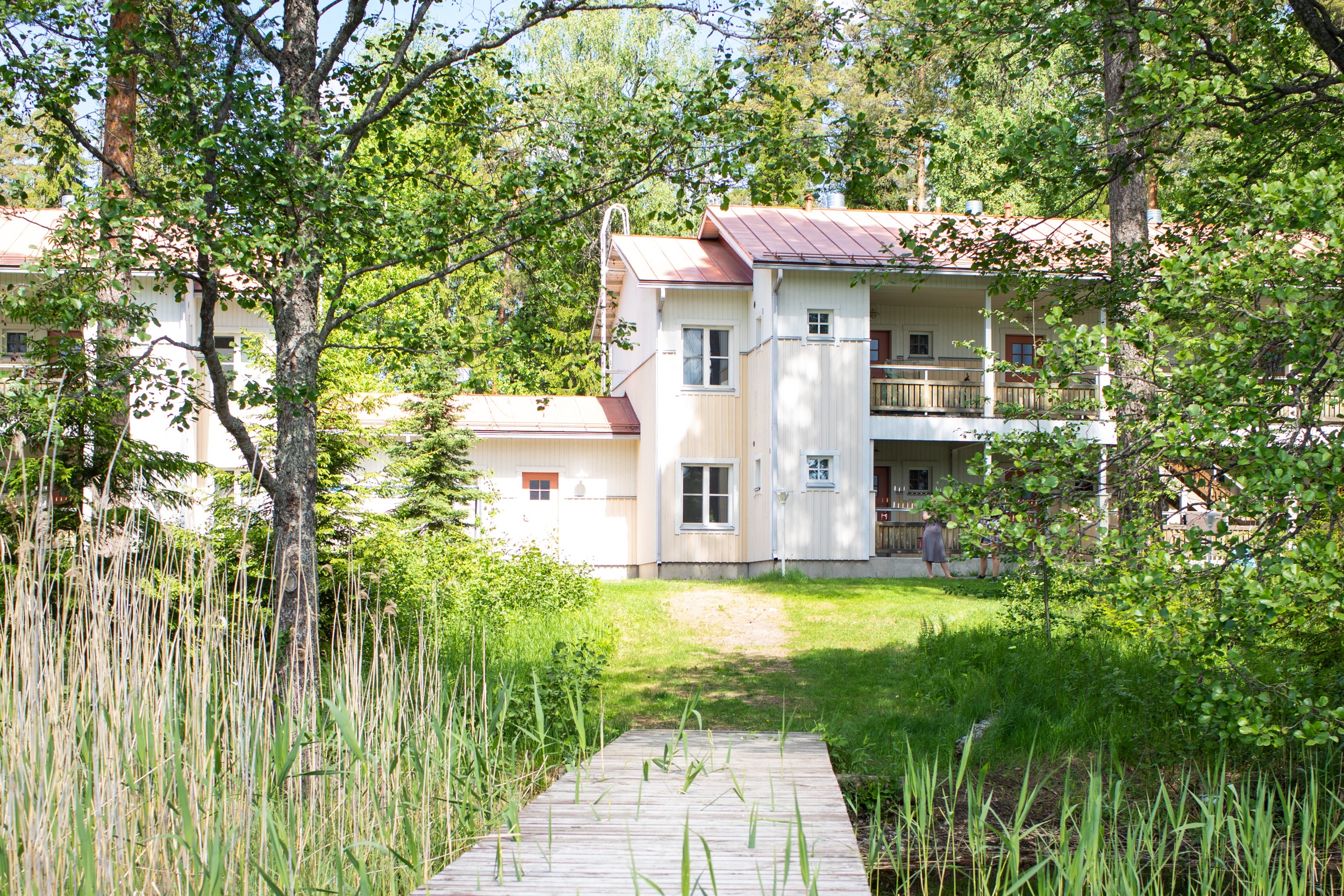 Kaksi kerroksinen, keltainen puutalo järven rannalla. 