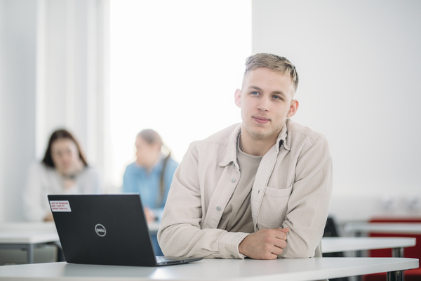 A person is looking ahead and sitting by a table with his laptop.