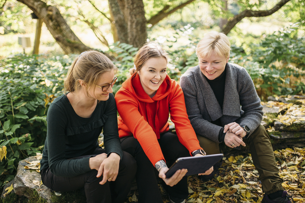 Three persons are sitting at a log at forest and smiling.