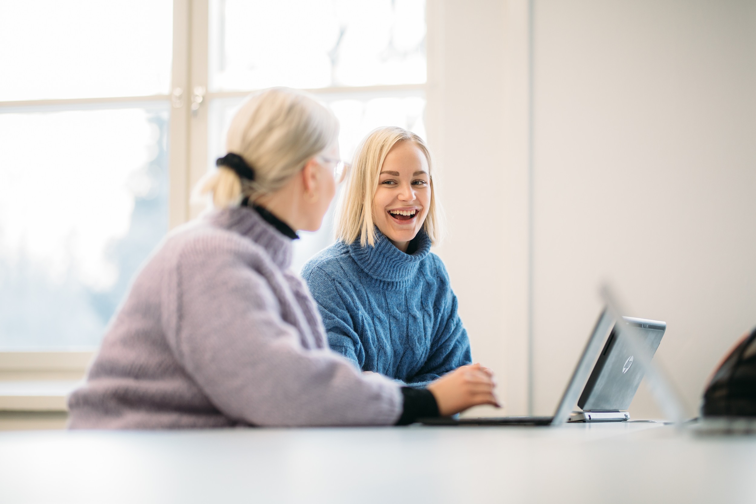 Two persons are sitting on a computer and looking each other.