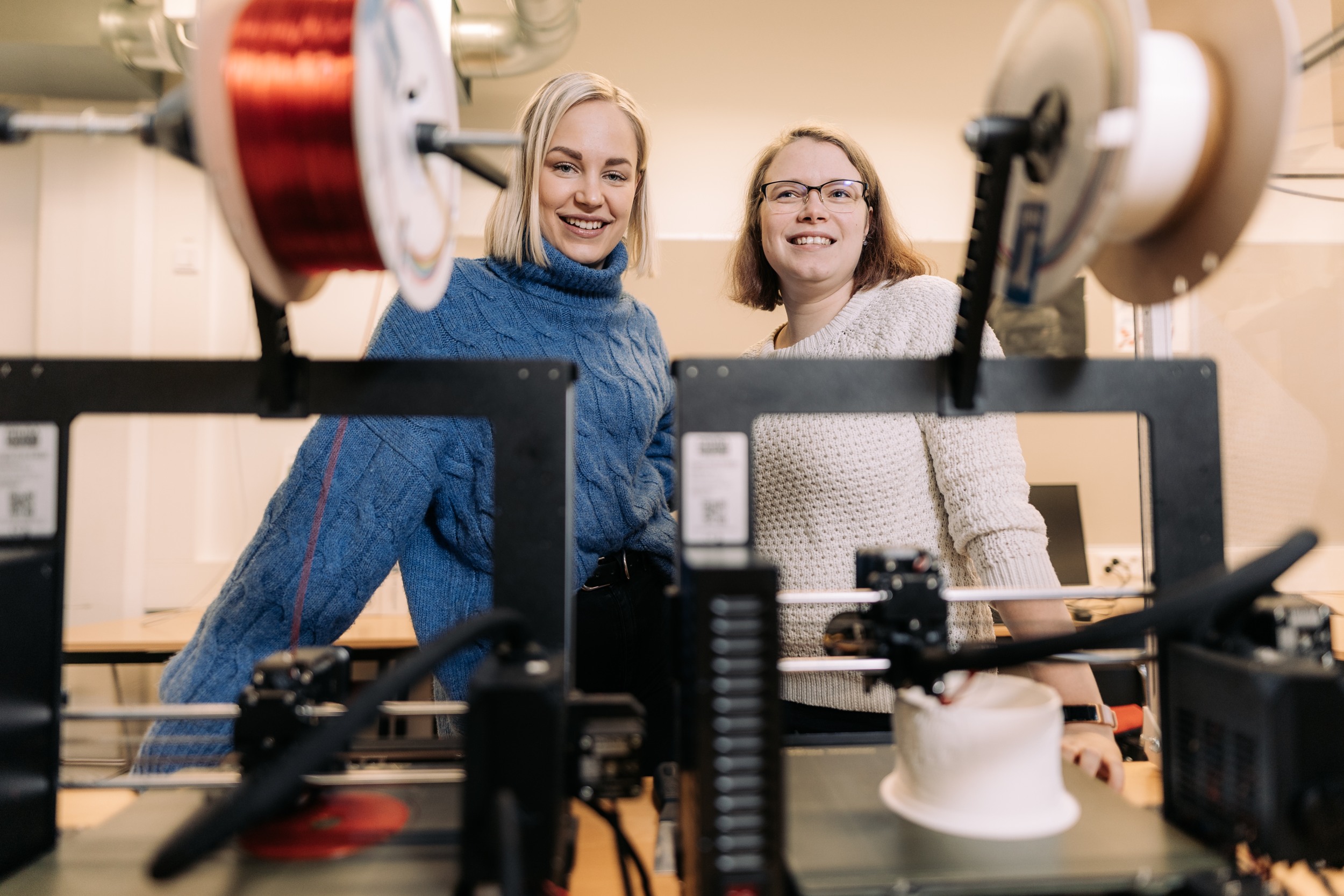 Two women looking to camera and standing front of the small machinery.