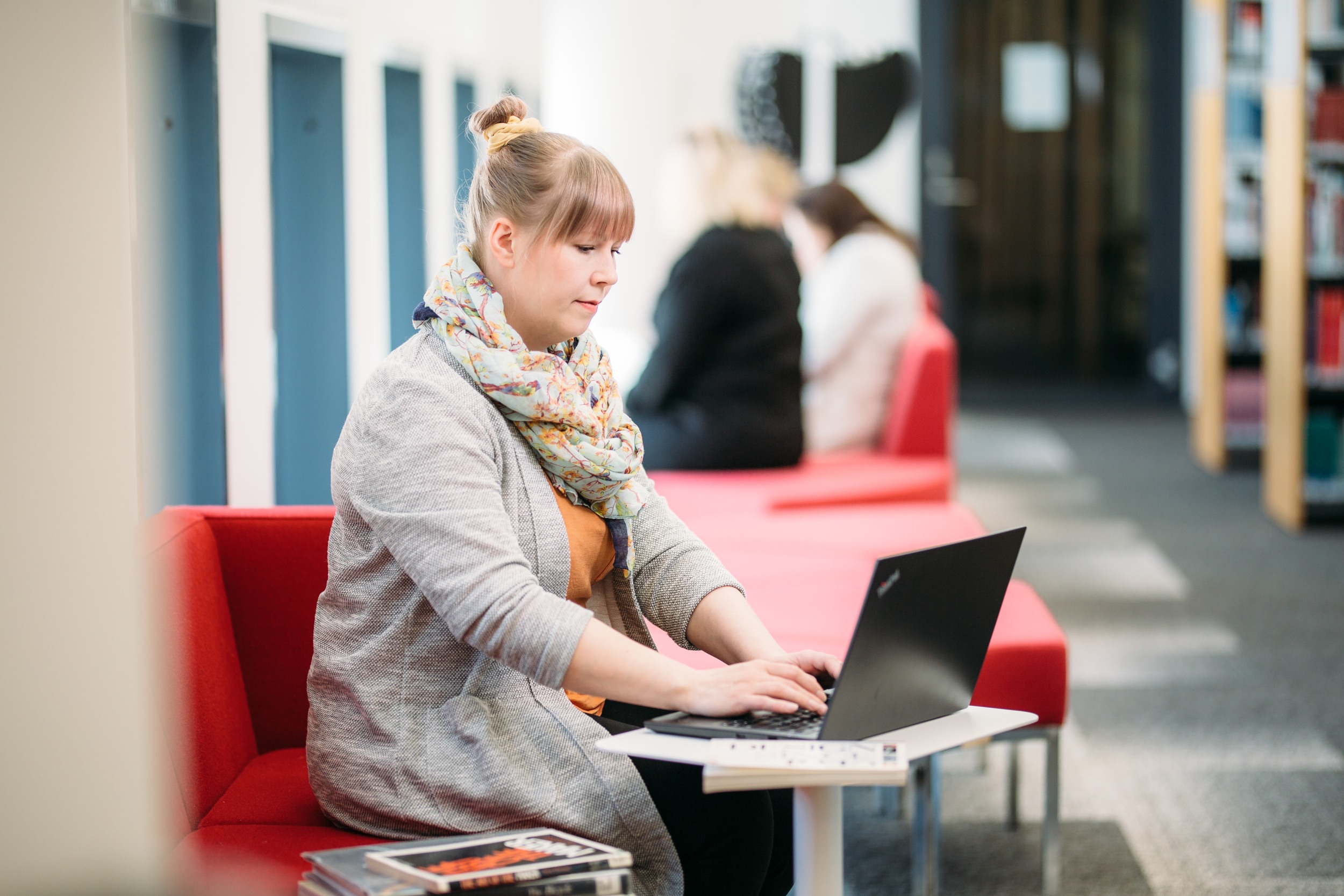 The person is sitting on a red couch and working at a desk with a laptop.