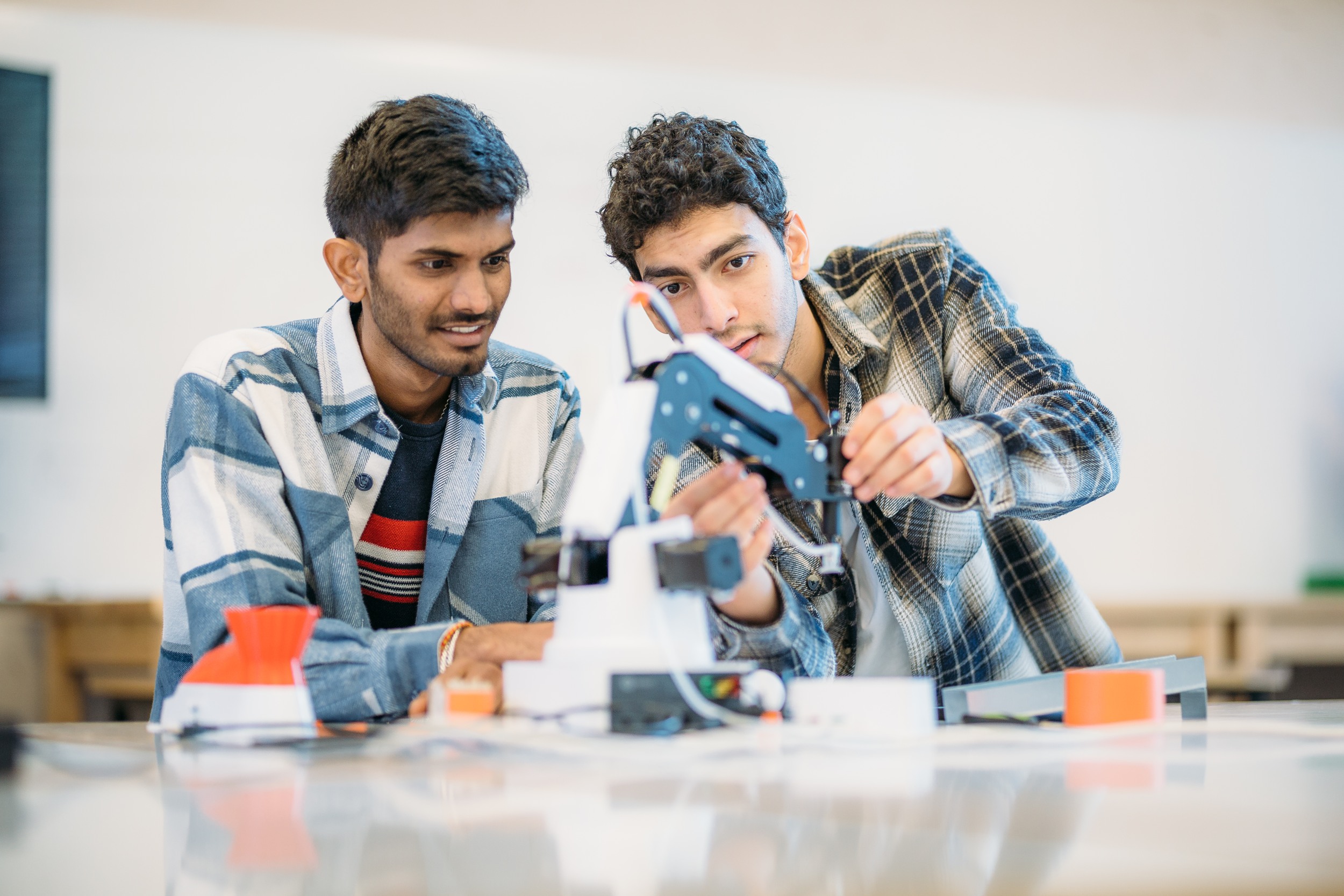 Two individuals are jointly examining a device with electric cables coming out of it.