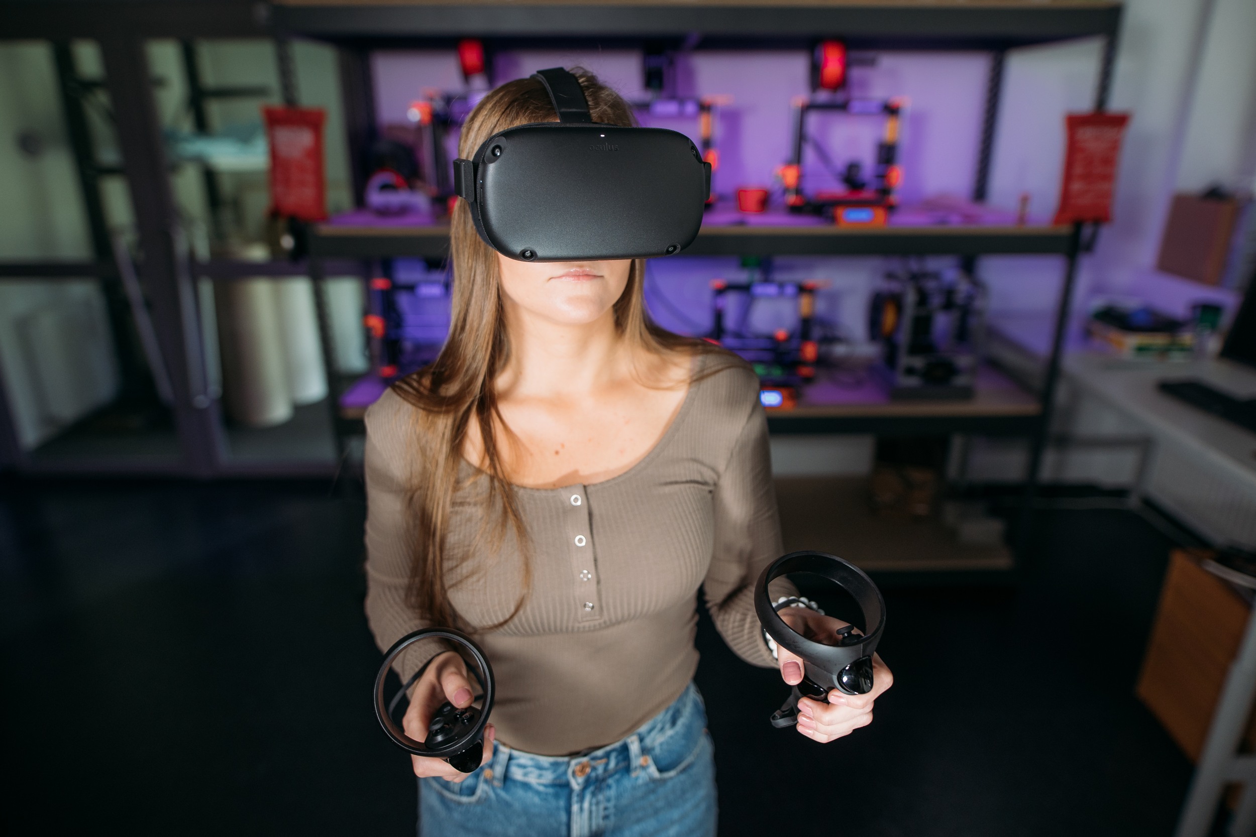 Opiskelija seisoo 3D-printtereiden edessä, päässään virtuaalilasit ja käsissään virtuaalilasien ohjaimet