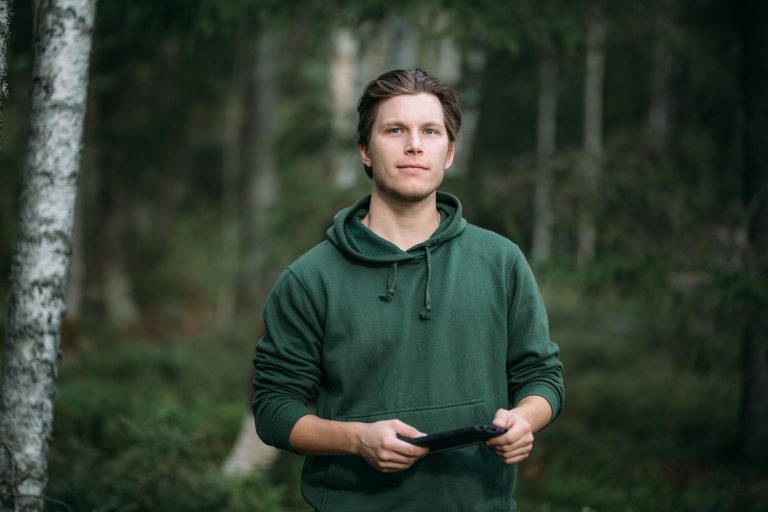 Henkilö seisoo metsässää vihreä huppari päällä.