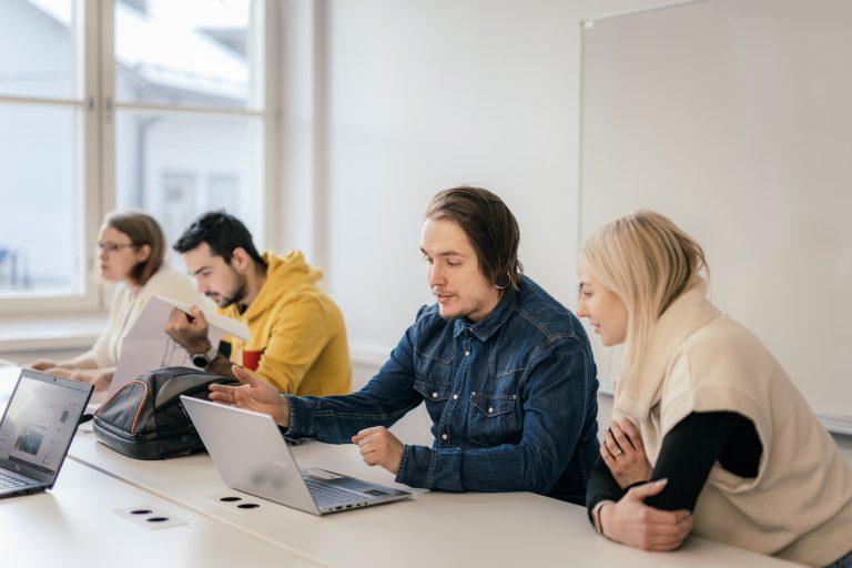 Ihmisiä istumassa pöydän ääressä kannettavan tietokoneen ääressä
