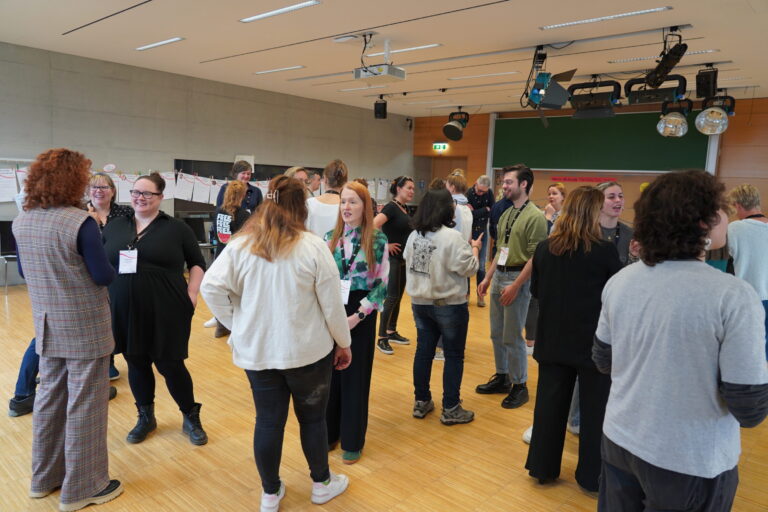 Persons standing and talking to each other in a room full of people