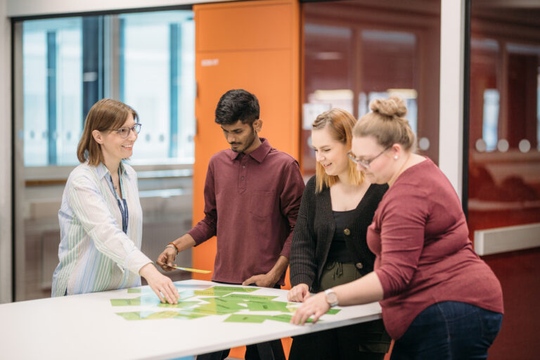 Four people gathered around a table/Kolme ihmistä kerääntynyt pöydän ääreen