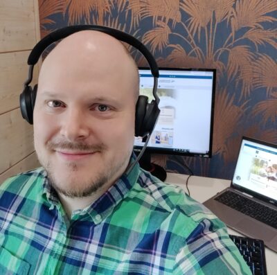Data-asiantuntija Ari Saari katsoo kameraan, taustalla kannettava tietokone ja näyttö.