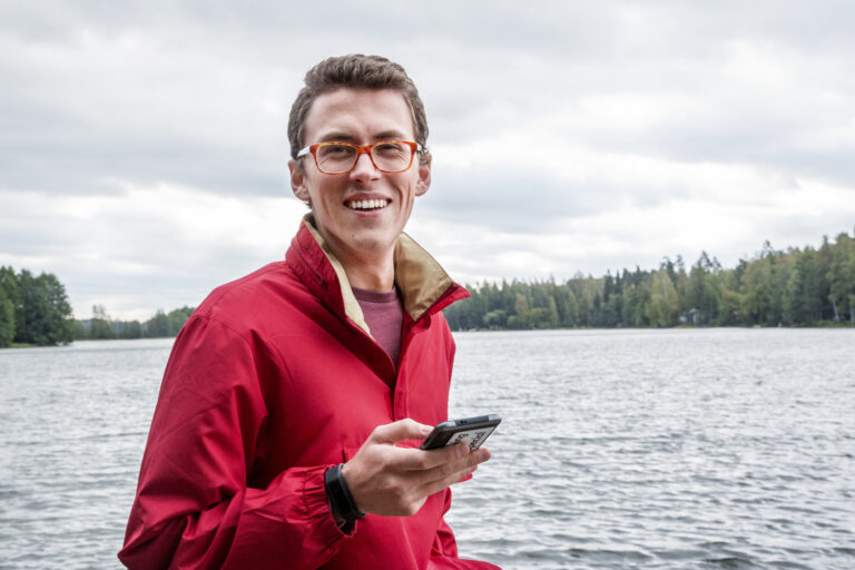 Poika on puhelimella järvenrannlla/ A boy on his phone next to a lake