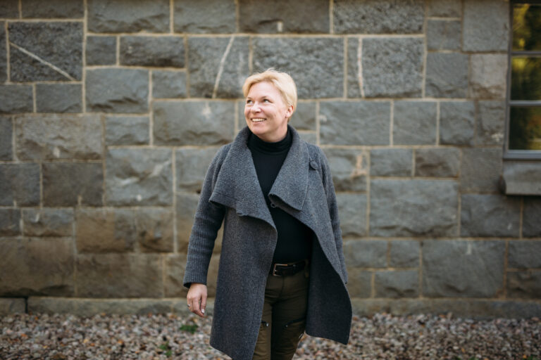 A woman smiling in front of a building/ Nainen hymyilee rakennuksen edessä .