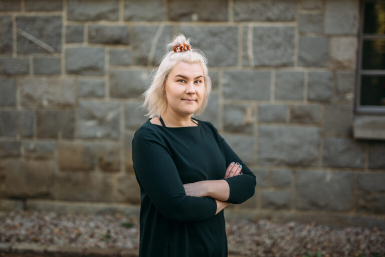Nainen seisoo rakennuksen edessä/ A woman is standing in front of a building