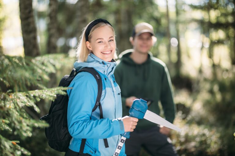 Naisopiskelija metsässä mittauslaite kädessä