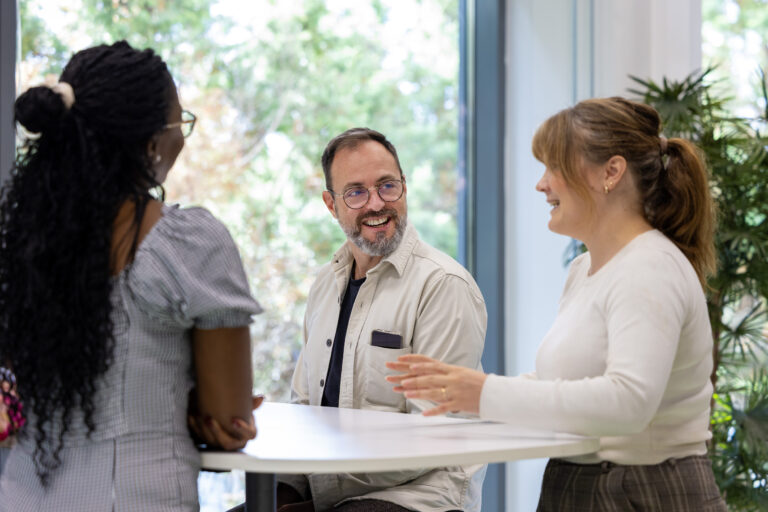 Ryhmä ihmisiä, jotka seisovat pöydän ympärillä keskustelemassa.