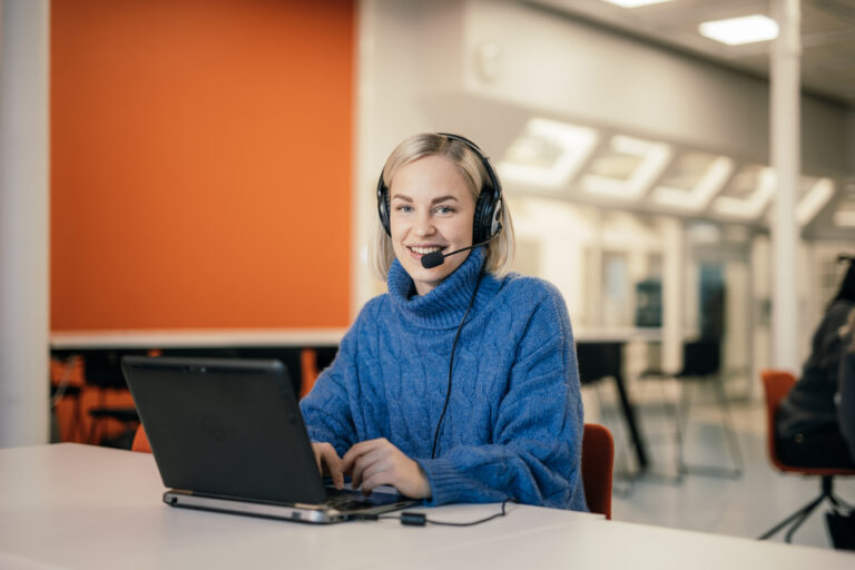 Nainen istuu tietokoneella kuulokkeiden kanssa/ Woman is sitting on a computer with headphones