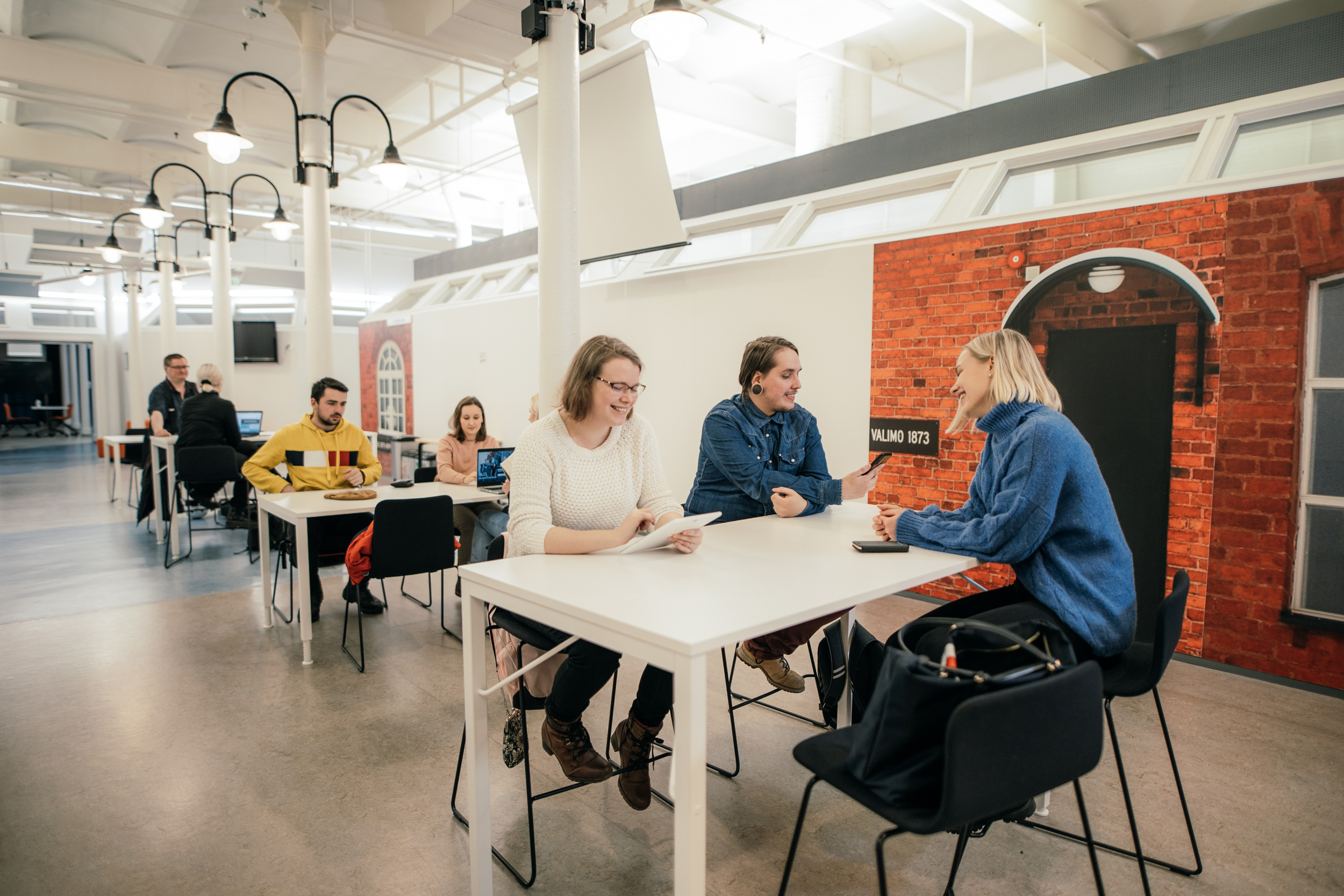 Ihmisiä istuu pöytien ääressä/People sitting around tables. 