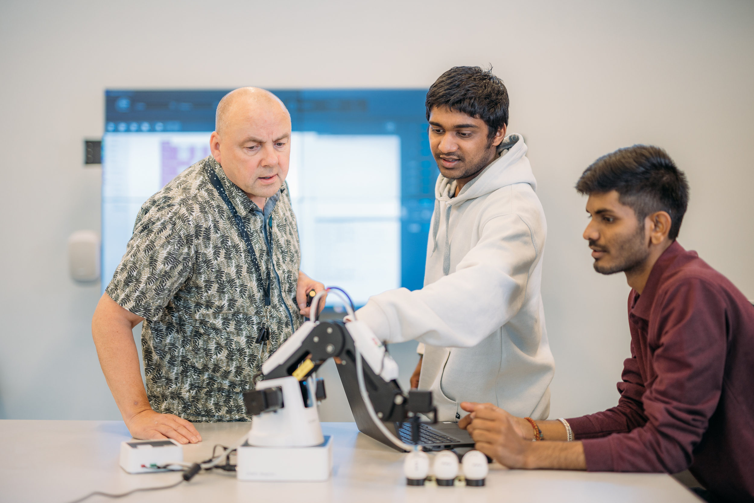 Three people looking at a machine/ Kolme ihmistä katsoo konetta