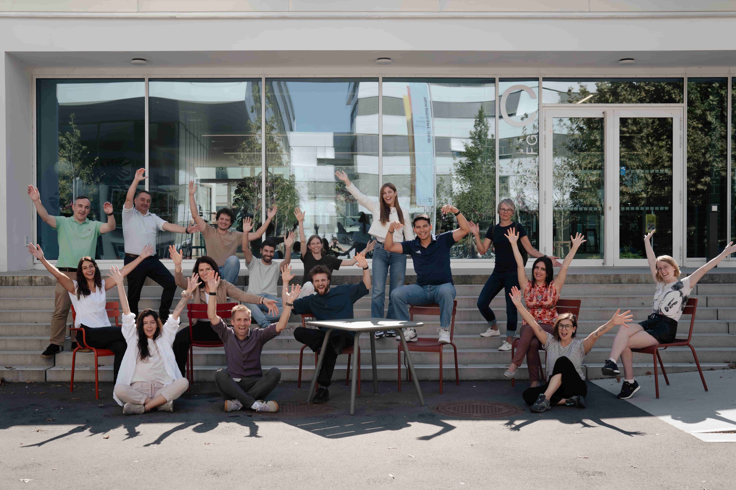 Lähes parikymmentä henkilöä ovat ulkona aurinkoisessa säässä, hymyilevät ja pitävät käsiään ylhäällä