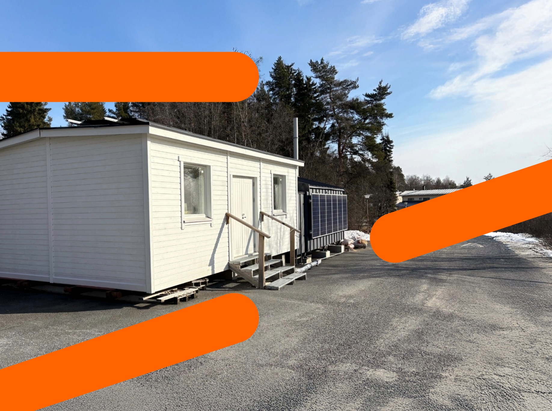 Valkoinen konttirakennus ulkona, jonka etuosassa portaat ovelle ja kaksi ikkunaa. Taustalla puita ja sininen taivas.