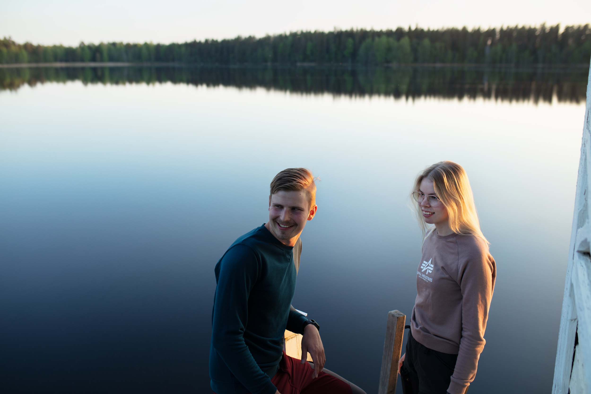 Kaksi ihmistä hymyilee järven vieressä/ Two people are smiling next to a lake