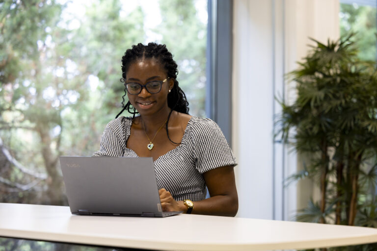 Nainen istuu pöydän ääressä ja käyttää kannettavaa tietokonetta.