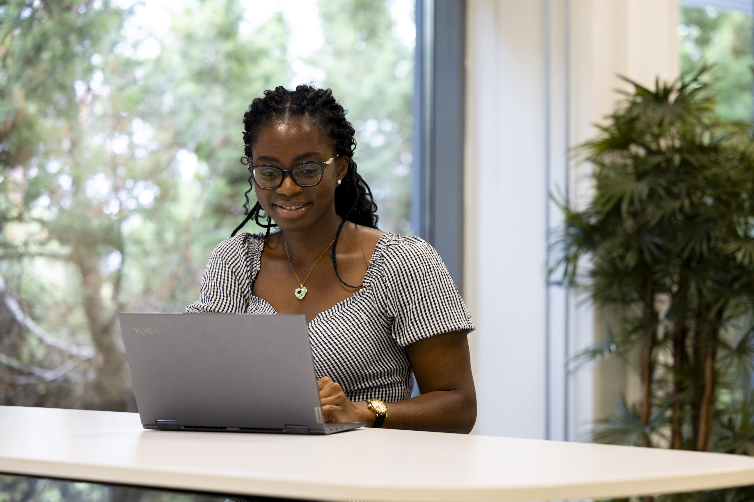 Nainen istuu pöydän ääressä ja käyttää kannettavaa tietokonetta.