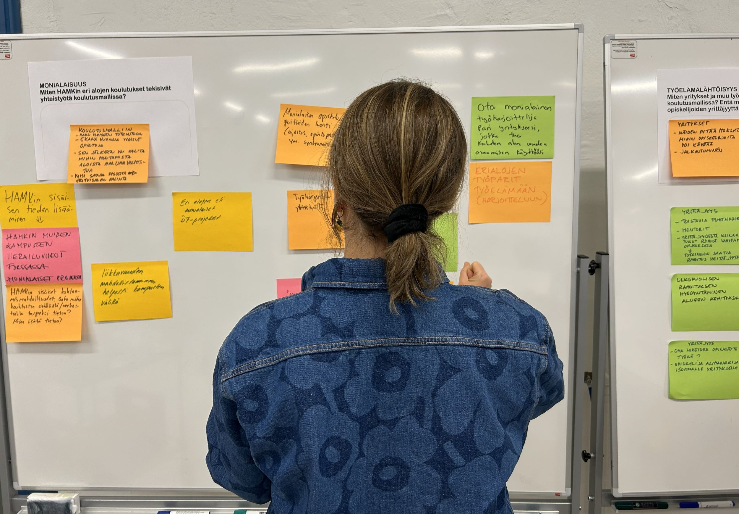 Nainen työpajassa ilmoitustaululla, selin kameraan