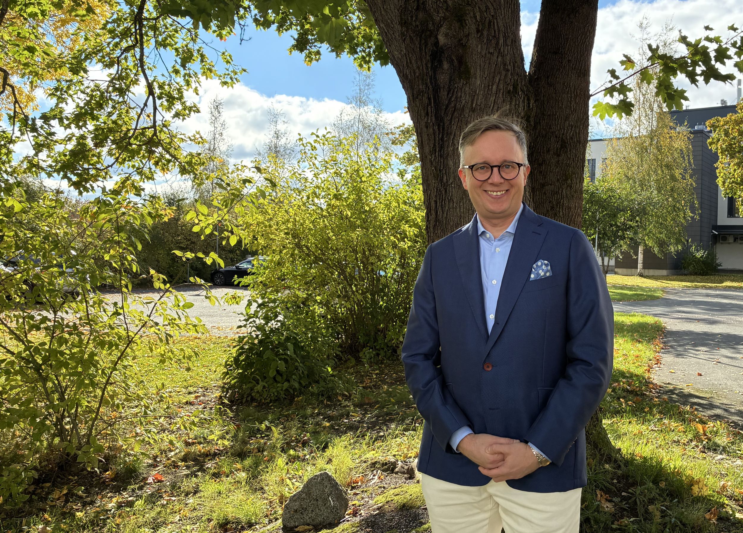 Sami Löfgren hymyilee puun varjossa kesäisessä maisemassa.