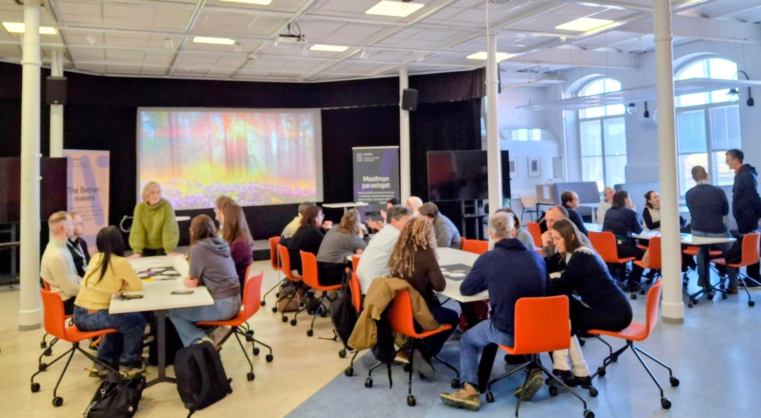 Joukko ihmisiä pöytien ympärillä istumassa Forssan kampuksella.