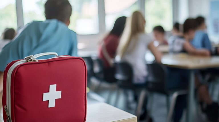 Ensiapulaukku kuvan etualalla vasemmalla. Takana opiskelijoita luokkatilassa.