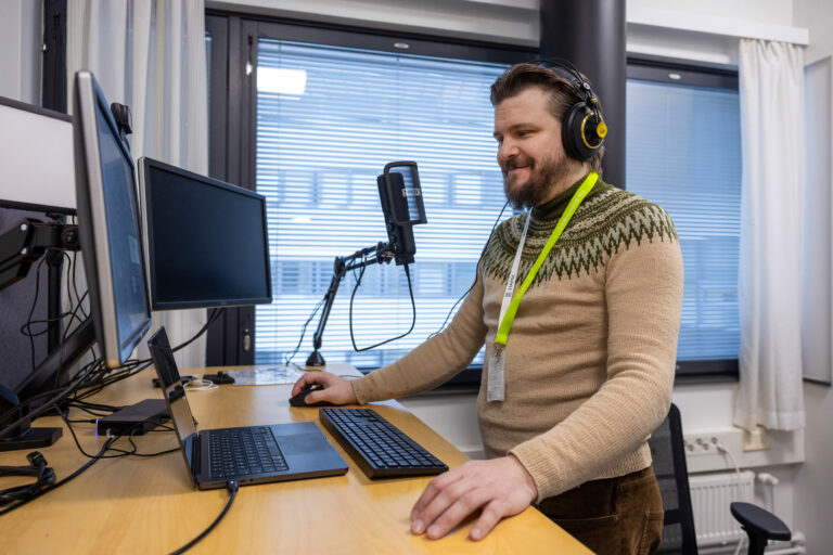 Mieshenkilö työskentelee tietokoneen ääressä kuulokkeet korvilla