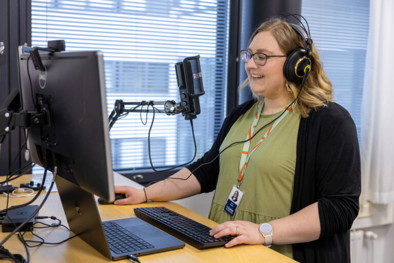 Nainen työskentelee tietokoneella kuulokkeet korvilla.