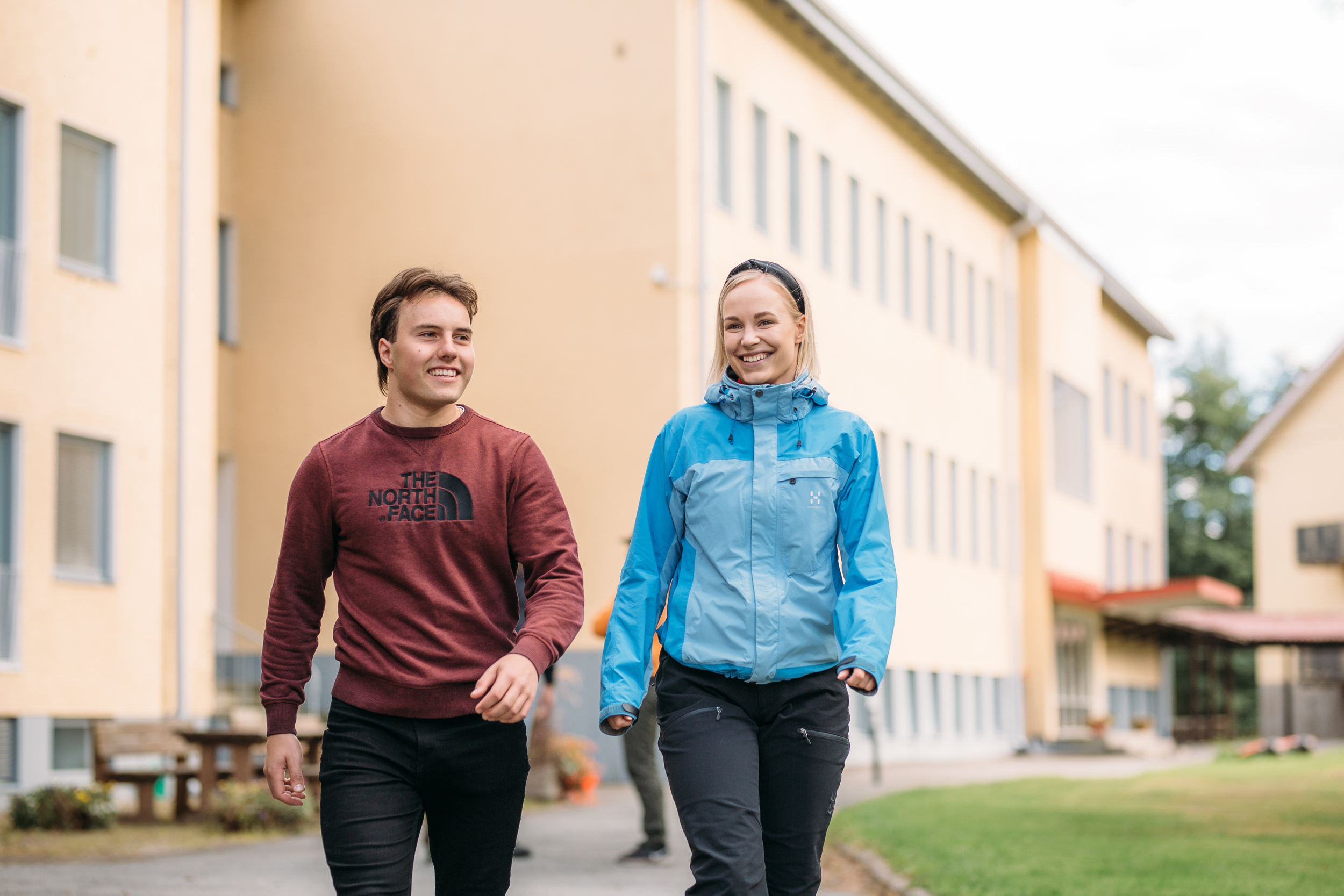 Two people walking outside of a building/ Kaksi ihmistä kävelee rakennuksen ulkopuolella
