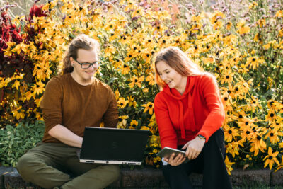 Two people outside with their laptops/ Kaksi ihmistä tietokoneilla puutarhassa