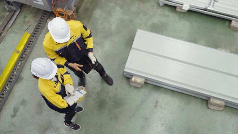 Top view of industrial engineers men and women wearing safety hard hat standing in plant while working and discuss together at metal manufacturing factory