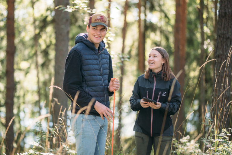 Two people smiling in a forest/Kaksi ihmistä hymyilee metsässä