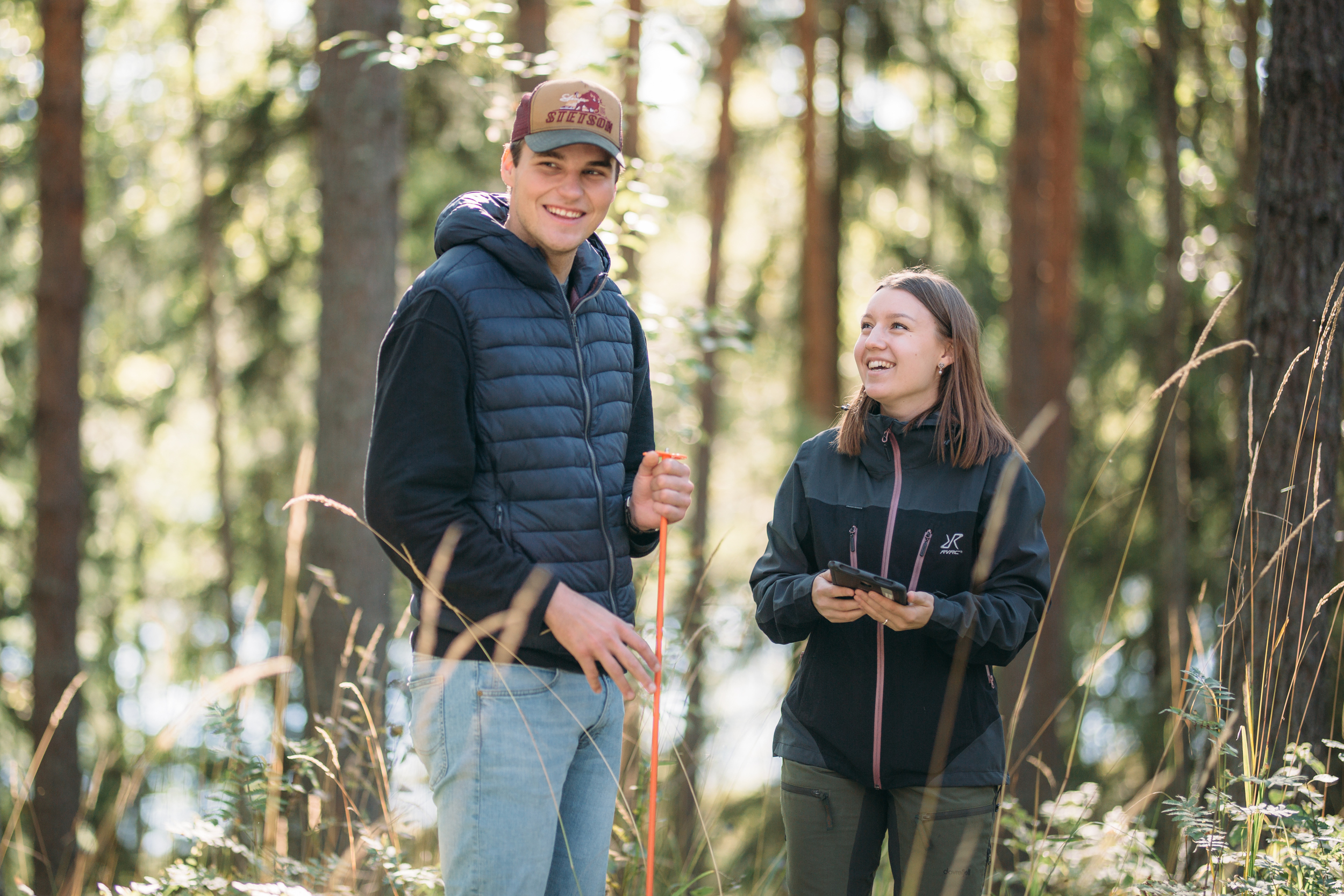 Two people smiling in a forest/Kaksi ihmistä hymyilee metsässä